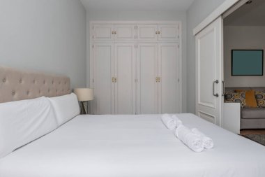 Çift kişilik yatak odası, döşenmiş yatak başlığı ve sandıklı gardırop ve beyaz ahşap kapılar.