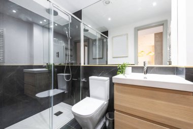 Üzerinde beyaz porselen lavabo olan banyo. Ahşap dolapta asılı. İki çekmece siyah mermer döşemeli banyo.