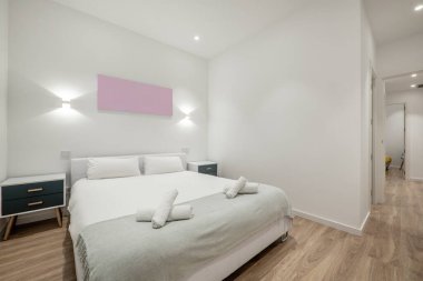 Çift kişilik yataklı, gri battaniyeli ve rulo havlulu bir yatak odası, gardırop, siyah masalar ve kiralık bir apartmanda ahşap zemin.