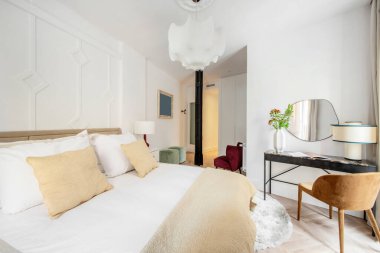 Büyük boy ahşap, beyaz yatak odası, beyaz ve krem yastıklar, siyah masa ve döşenmiş kahverengi ahşap sandalye.