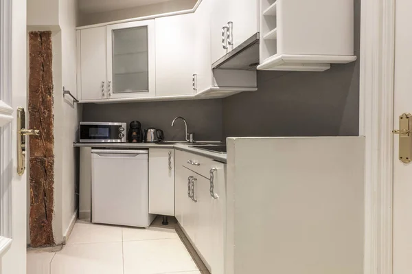 厨房的一角 有白色的木柜 一个玻璃柜 一个灰色的台面 一个白色的小冰箱和一个微波炉 柜台上有一个水壶 — 图库照片