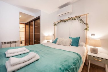 Balyaları olan ahşap yatak odası, koyu ahşap gardırop, klima, süit tuvalet, beyaz alüminyum radyatör, tatil için kiralanan yatağın üzerinde havlular.