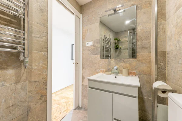 bathroom with white porcelain on white wooden sink with frameless mirror, marble tiling and chrome heated towel rail in vacation rental apartment