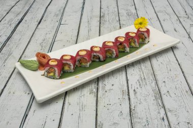Kırmızı ton balığıyla kaplı uramaki suşisi tepsisi ve soslu avokado ile doldurulmuş masago yumurtası, muz yaprağı, Norveç yosunu, zencefil ve wasabi.