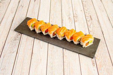 Norveç somonuyla kaplı bir porsiyon uramaki suşisi tepsisi ve sosla doldurulmuş avokado, masago roe, siyah bir tepside Norveç yosunu.