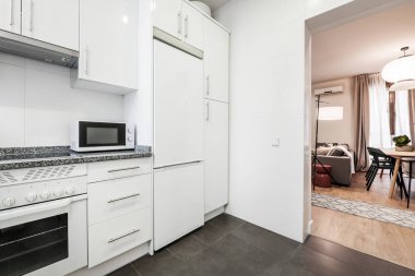 Eşleşen aletleri olan beyaz mutfak, gri granit tezgah, beyaz mikrodalga fırın ve oturma odası ve yemek odası.