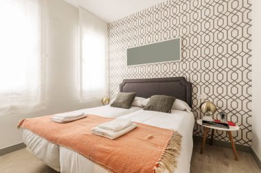 Çift kişilik yatak odası, beyaz yastıklar, kahverengi yastıklar ve kısa süreli kiralık bir dairede battaniyenin üzerinde katlanmış havlular.