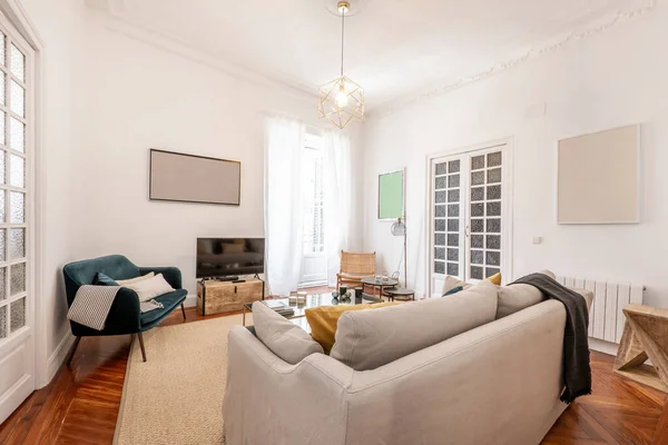 Üç koltuklu oturma odası, kumaşla döşenmiş bir sürü yastık, beyaz kapılı balkon ve kapılarında marangozluk, yerde hafif halı ve bir duvarda televizyon.