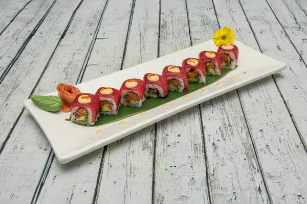 Kırmızı ton balığıyla kaplı uramaki suşisi tepsisi ve soslu avokado ile doldurulmuş masago yumurtası, muz yaprağı, Norveç yosunu, zencefil ve wasabi.