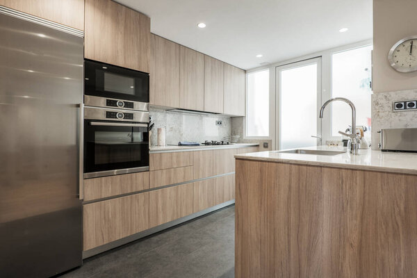 Kitchen with oak furniture, integrated appliances, white stone countop and dark stoneware floor and access to a glazed terrace