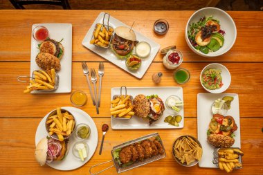 Karışık hamburgerler, keçi peyniri salatası, nachos, turşu, patates kızartması, tavuk madalyonu, soslar, guacamole