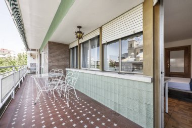 Beyaz boyanmış demir bir masa ve kil renkli terrazzo zeminli cam kapağı olan büyük bir teras.