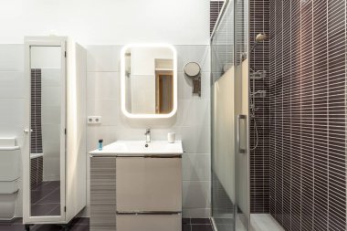 bathroom with one-piece white porcelain sink on lacquered wood cabinet with drawers, wall-mounted frameless square mirror and glass-enclosed shower stall