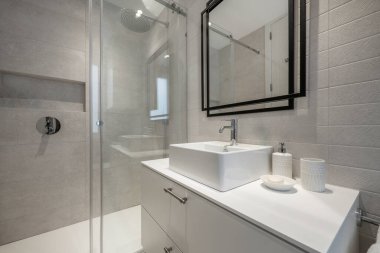 Siyah metal bir yapı ve duş kabini üzerinde ayna olan tek parça kare porselen bir lavabosu olan beyaz ahşap bir lavabo.