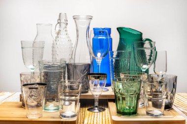 Cam bardaklar, bardaklar, sürahiler ve şişeler ahşap masada.