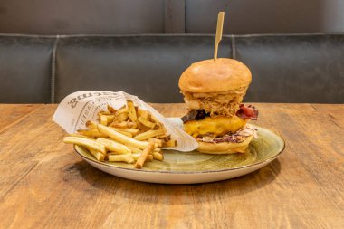 Domates, marul, erimiş çedar peyniri, kızarmış domuz pastırması, kızarmış soğan halkaları, peynir ve ahşap bir masada büyük porsiyon ev yapımı patates kızartması ile çok katmanlı çıtır sığır eti ve tavuk burger.