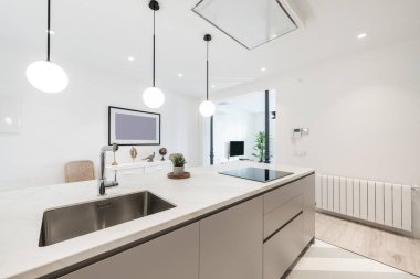 Mutfak adası, krom musluğu olan paslanmaz çelik lavabo, siyah seramik hob ve çıkarıcı kaput, beyaz alüminyum radyatör ve küresel laleli lambalar.