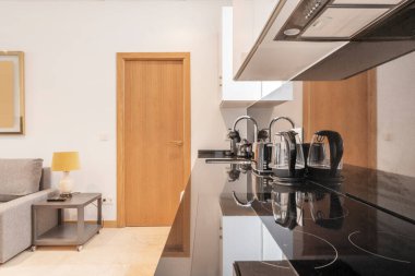 open plan kitchen with black marble top with small appliances, four burner ceramic hob, fabric sofa and gray side table