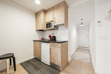 Koyu gri tezgahlı mutfak, ahşap dolaplar ve kiralık bir apartman dairesinde, bir antredeki koridorun yanına yerleştirilmiş beyaz eşyalar.