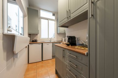 Koyu yeşil ahşap dolapları, beyaz aletleri, ahşap tezgahı ve beyaz çerçeveli servis kapağı olan mutfak.