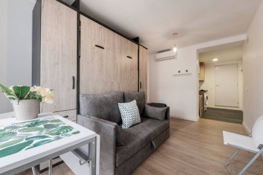 Kısa süreli kiralık stüdyo dairesi olan kanepenin içinde ekstra yatak. Gardıroplu, beyaz ahşap masa, sandalyeler ve parke döşeme.