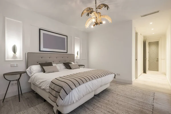 Çift kişilik yatak odası, bej kumaş yatak başlığı battaniye ve halıyla birleştirilmiş, ahşap döşeme ve çift yataklı yataklar.