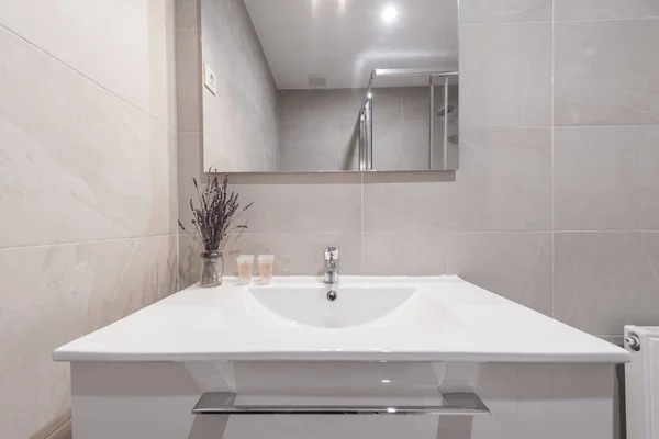 Photo of Bathroom front with beige paneling and frameless wall mounted mirror, white porcelain sink above vanity and chrome fixtures