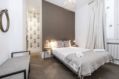 bedroom with armchair, double bed with cushions, rolled towels and decorative paper on the walls