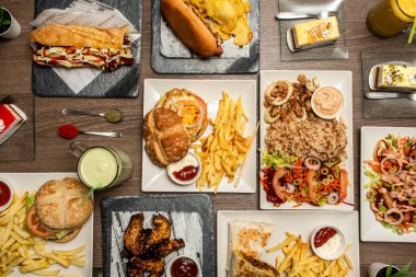 Fast food dishes with basmati rice with squid, hot dogs, assorted burgers, sandwich with sauce and fries, desserts and cakes, barbecue wings