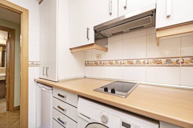 Beyaz ahşap dolaplı mutfak ve ahşap tezgahlı entegre beyaz eşyalar, çekmeceler ve kiralık tatil dairesindeki valans.