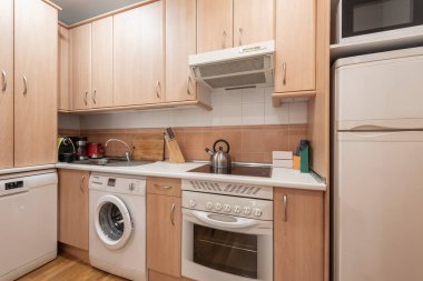 Hafif ahşap mobilyalı, entegre beyaz aletli mutfak, uyumlu buzdolabı, fırın ve bulaşık makinesi, küçük aletli beyaz tezgah.