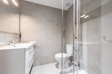 Tek parça reçine lavabosu olan banyo, çerçevesiz ayna kaplamaları ve krom armatürleri olan duş kabini.