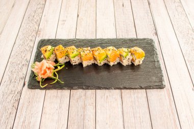 Avokado, Japon pilavı, susam, haşhaş, zencefil ve wasabi içeren bir porsiyon somon uramaki suşisi içeren siyah tahta tepsi.