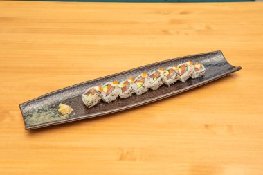 Avokado, masago roe, nori deniz yosunu, Japon pilavı, susam ve haşhaş tohumu, zencefil ve wasa içeren bir porsiyon somon uramaki sushi ile modern tarz siyah tepsi.