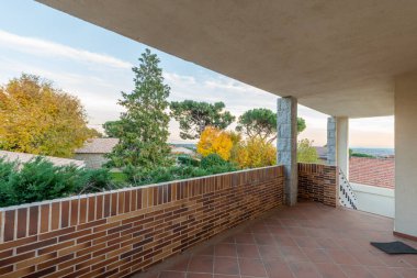 Aynı malzemeden yapılmış merdiveni ve kırsal manzaralı tuğla duvarı olan teras zeminli tek kişilik bir evin verandası.