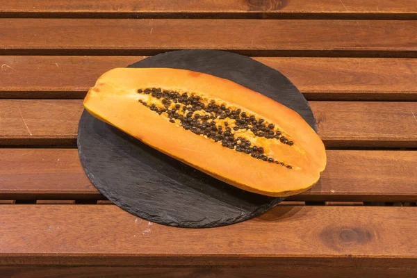Half ripe canarian papaya on round black slate plate and wooden board table