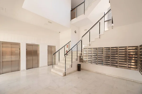 Lobby of a building with an atrium, stairs with metal and glass railings, stainless steel mailboxes and a battery of three elevators