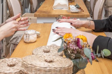 Kuru çiçeklerin yanındaki ahşap masaya koyu kırmızı bir kılıfla bir kadının ellerini boyamak.