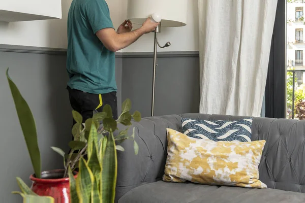 Operator changing a light bulb in a lamp in the living room of a house