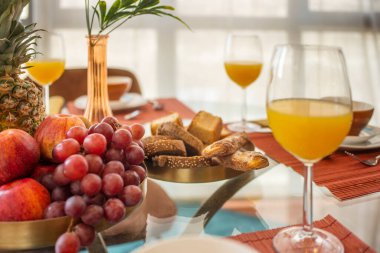 Centerpiece with tray of fresh fruit, bunch of grapes, lots of muffins and sweets, decorative vase, red apples, ripe plums and glasses of orange juicef