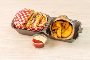 Huge hamburger with everything wrapped in paper with sauces and cone with fries wedges