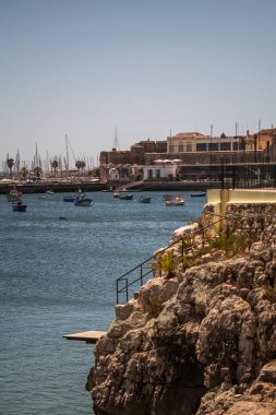 Cliff with railing down to a diving board next to a marina in the sea