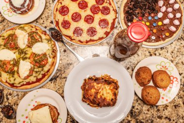Set of fast food dishes, mainly assorted pizzas, Venezuelan desserts and coffee on a red granite surface
