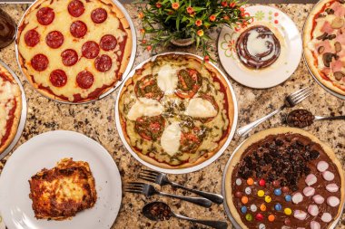 Set of fast food dishes, mainly assorted, pepperoni, cheese and tomato pizzas, Venezuelan desserts and coffee on a red granite surface