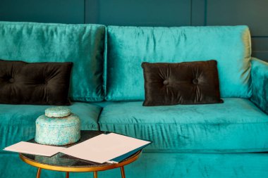 Mavi kadife koltuklu, yuvarlak camlı metal sehpalı ve mavi dekoratif kaseli bir stüdyo dairede oturma odası.