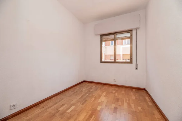 Empty living room with oak parquet floor, plain white walls and gold aluminum joinery on the windows