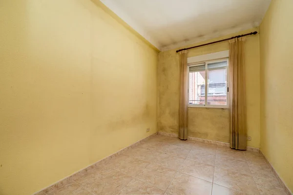 Empty room with yellow painted walls and a dirty one with curtains and pink stoneware floors