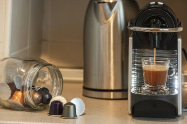 Kapsül kahve makinesi cam bir fincanda kahve ve kapsüllerle dolu bir şişe hazırlıyor.