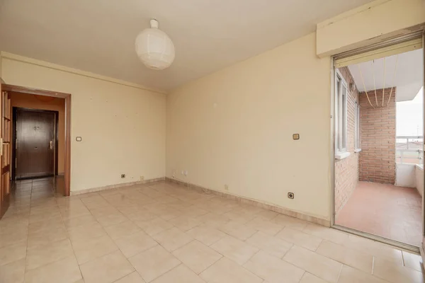 empty room has square tile stoneware floor, cream painted wall with gotelet, access to a terrace with clay floors and reddish wooden door with glass window