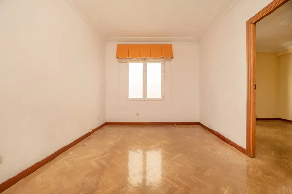 the empty room has herringbone oak parquet flooring, plain white painted walls, white aluminum window and orange skirting